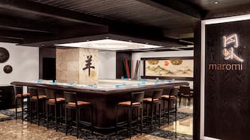 A modern bar area with a long counter, multiple stools, and a decorative wall with calligraphy.