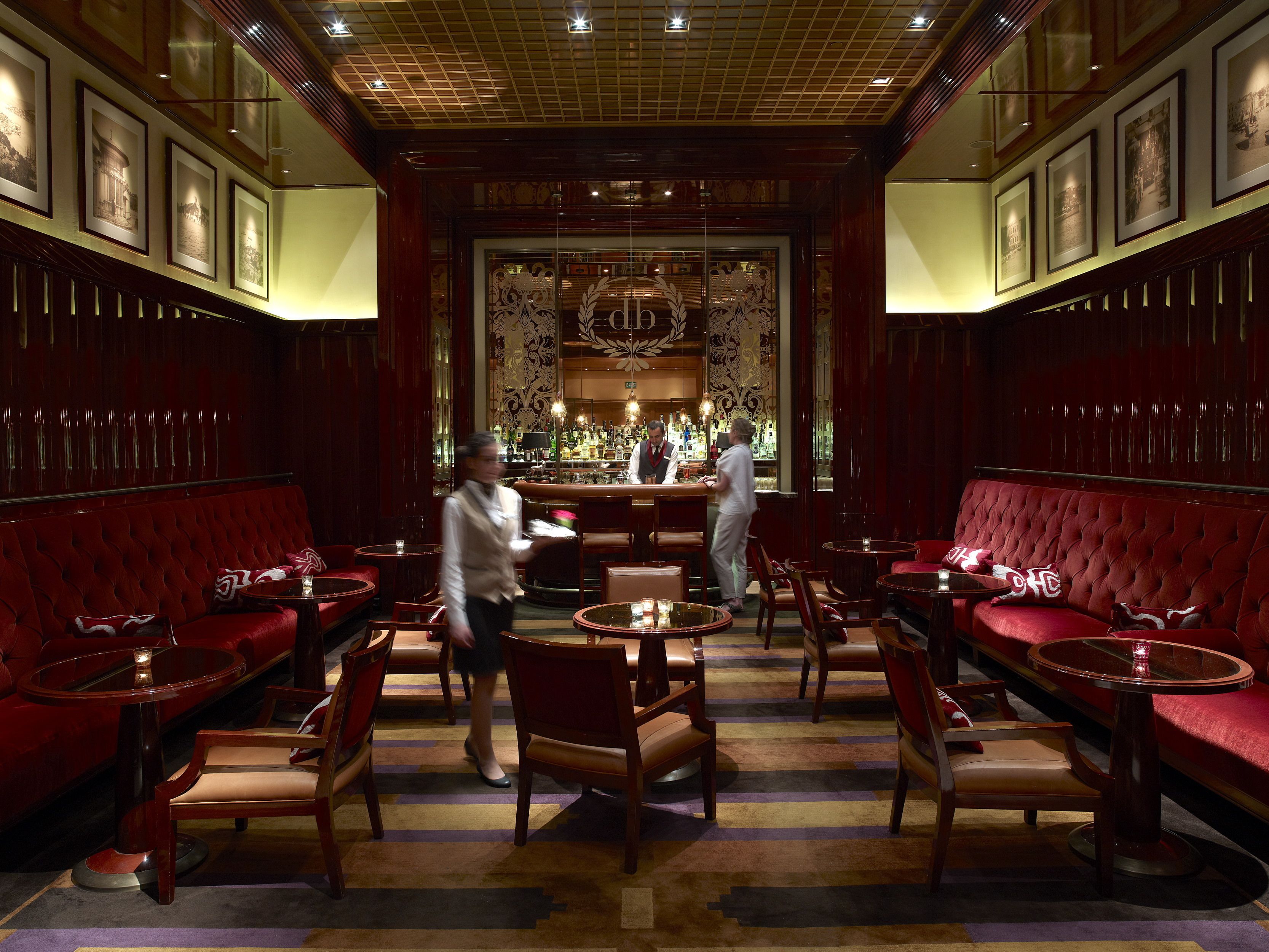 A luxurious bar area with red upholstered seating, wooden tables, and a bar counter.