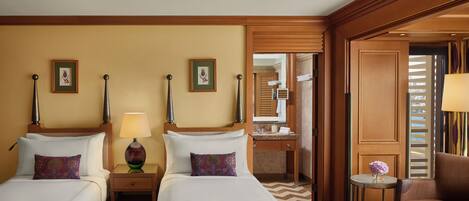 Een hotelkamer met twee bedden, een klein tafeltje met een vaas, een stoel en een zichtbare badkamer door een geopende deur.