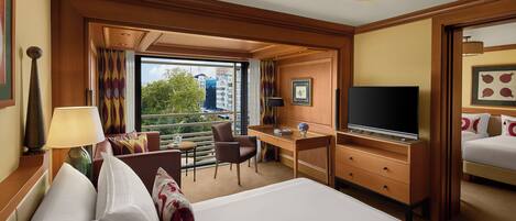 A hotel room with a large bed, a desk, a television, and a view of the city.