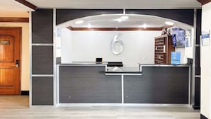 A reception desk with a number '6' sign, a security camera, and a blue informational poster. - Studio 6 Irving, TX – DFW North (Irving)
