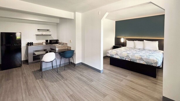 A modern hotel room with a bed, a desk, and a kitchenette. - Studio 6 Irving, TX – DFW North (Irving)
