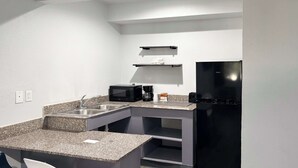 A compact kitchen with a granite countertop, a black refrigerator, a microwave, and a coffee maker. - Studio 6 Irving, TX – DFW North (Irving)