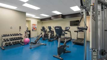 Ein Fitnessstudio mit verschiedenen Trainingsgeräten, darunter Laufbänder, Crosstrainer und Kurzhanteln.