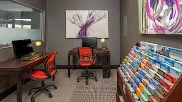 Un espace de bureau moderne comprenant un bureau, deux chaises de bureau, un ordinateur, une lampe et une bibliothèque remplie de livres de voyage.