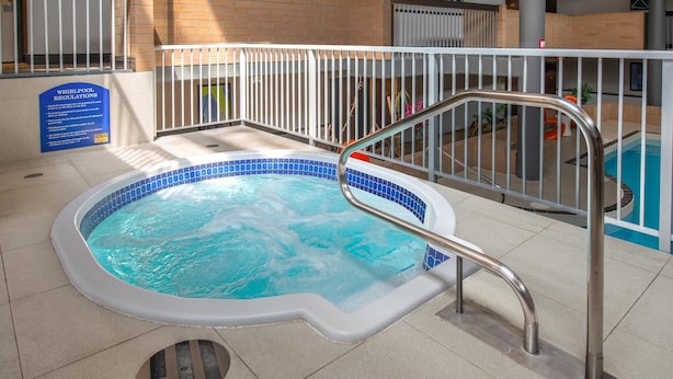 A hot tub with a metal railing, a sign with regulations, and a pool in the background. - Coast Calgary University Area Hotel by APA (Calgary)