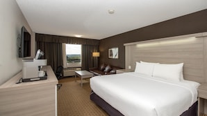 A hotel room with a large bed, a desk with a computer, a chair, a lamp, and a window with curtains. - Coast Calgary University Area Hotel by APA (Calgary)