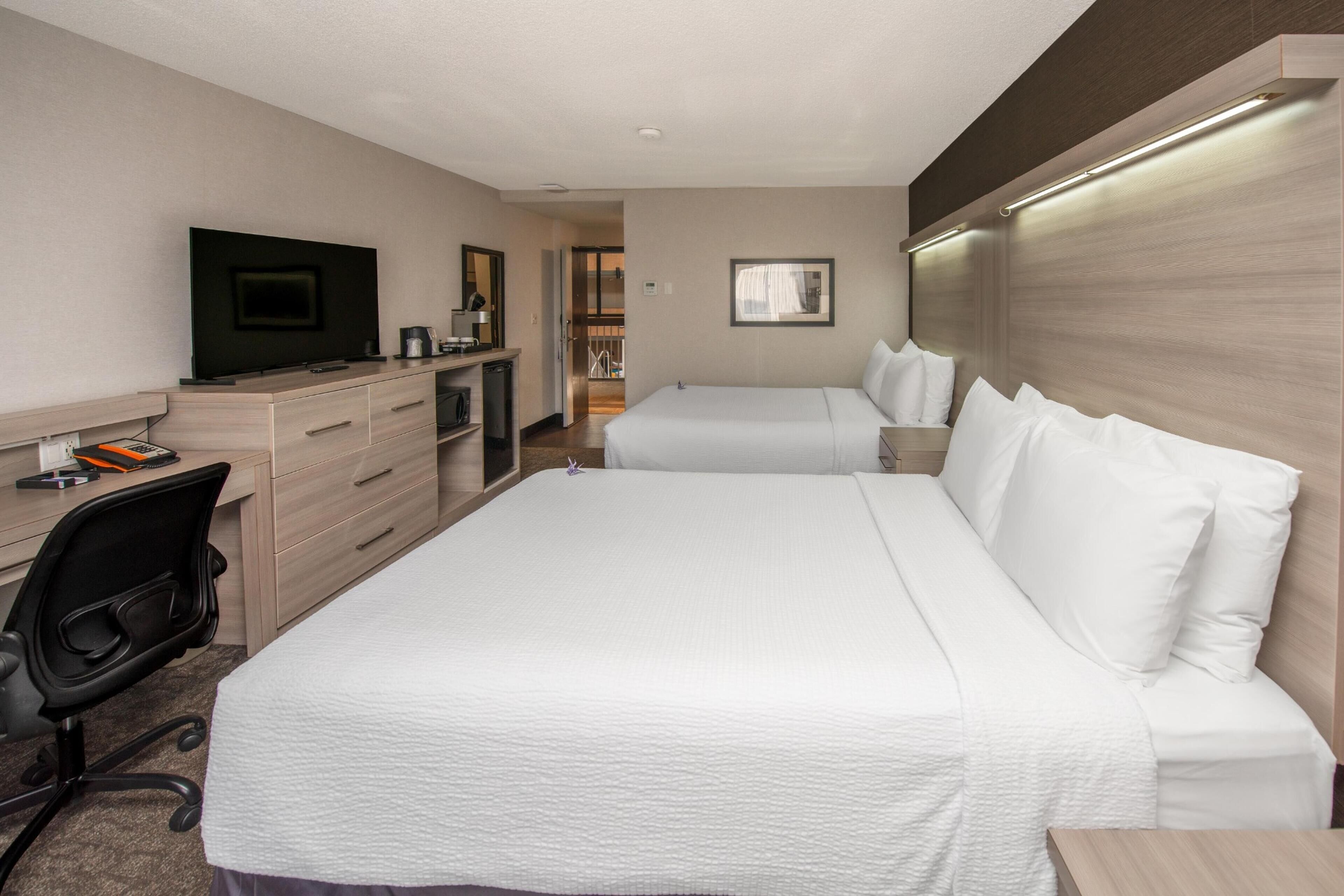 Habitación de hotel con cama, escritorio con ordenador, televisión y baño visible a través de una puerta abierta.