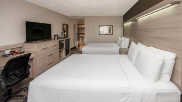 Habitación de hotel con cama, escritorio con ordenador, televisión y baño visible a través de una puerta abierta.