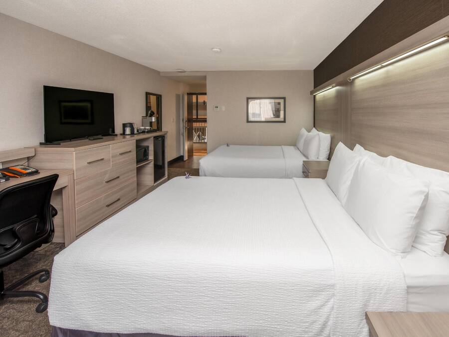 Habitación de hotel con cama, escritorio con ordenador, televisión y baño visible a través de una puerta abierta.