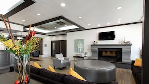 A modern living room with a fireplace, a sofa set, a round ottoman, and a flat-screen TV mounted on the wall. - Coast Calgary University Area Hotel by APA (Calgary)