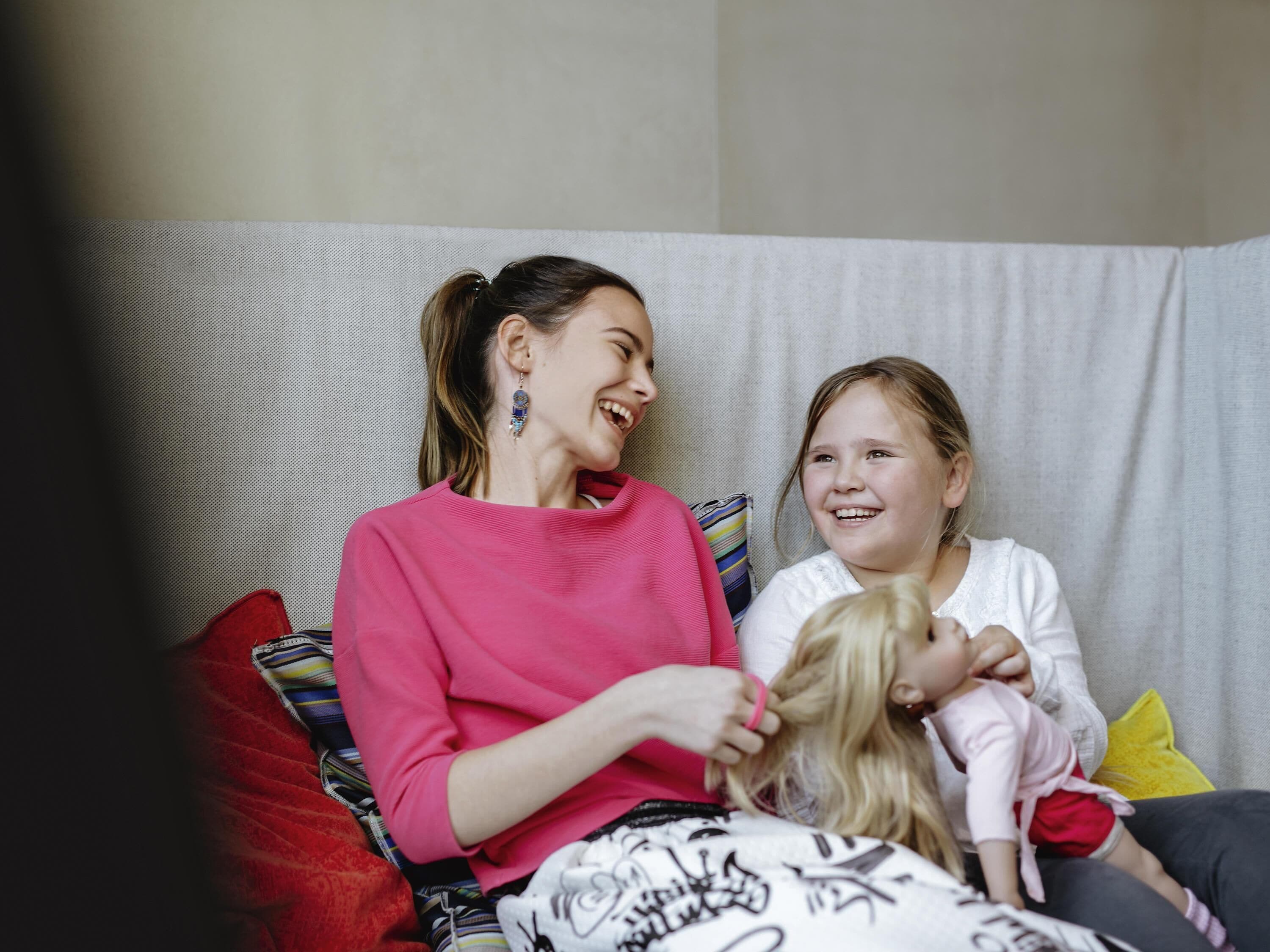 A person sitting on a couch with a child, a doll, and a patterned blanket.