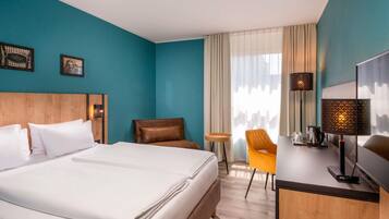 A hotel room with a bed, a desk, a chair, and a window with curtains.