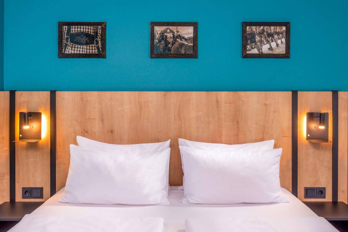 A hotel room with a wooden headboard, two white pillows, and three framed pictures on the wall.