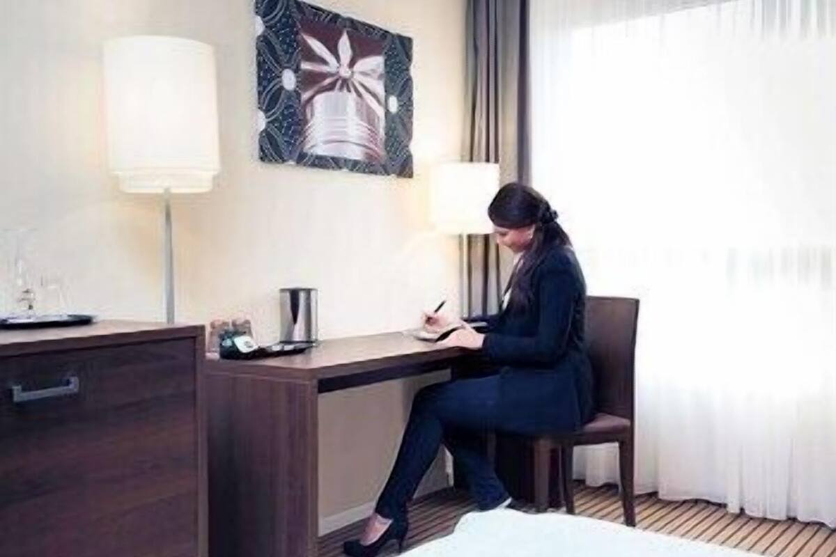 A hotel room with a desk, chair, lamp, and a bed.