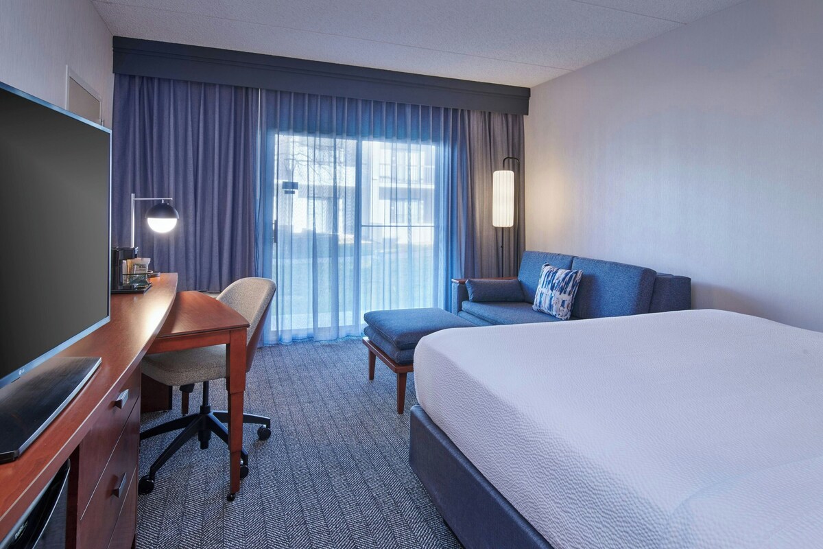 A hotel room with a large bed, a desk with a computer, a chair, a sofa, and a TV.