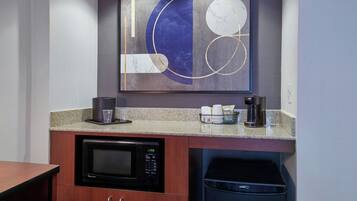A compact kitchen with a microwave, coffee maker, and trash bin.