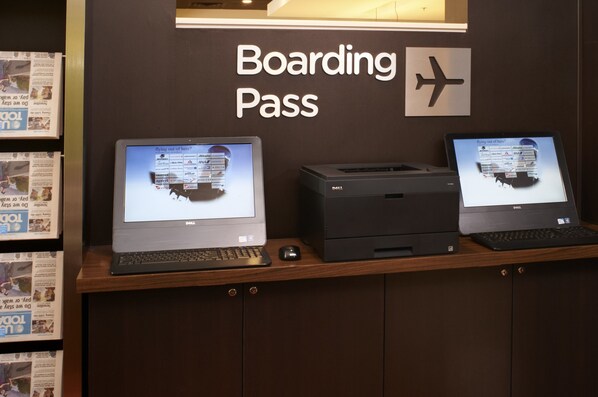 A desk with two Dell computers displaying boarding pass information, a printer, and a sign above reading "Boarding Pass" with an airplane symbol.