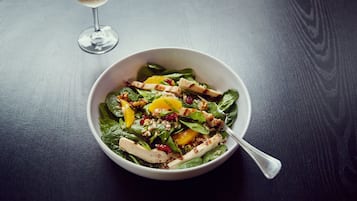 A bowl of salad with a fork on a dark wooden table.