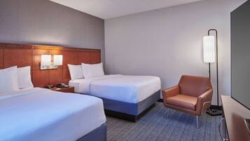 A hotel room with two beds, a desk, a chair, and a standing lamp.