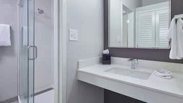Un baño moderno con cabina de ducha de vidrio, un lavabo blanco con espejo y un perchero para toallas.