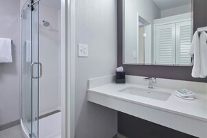Un baño moderno con cabina de ducha de vidrio, un lavabo blanco con espejo y un perchero para toallas.