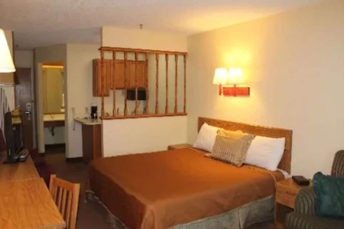 A hotel room with a bed, bedside table, lamp, and a view of the bathroom.