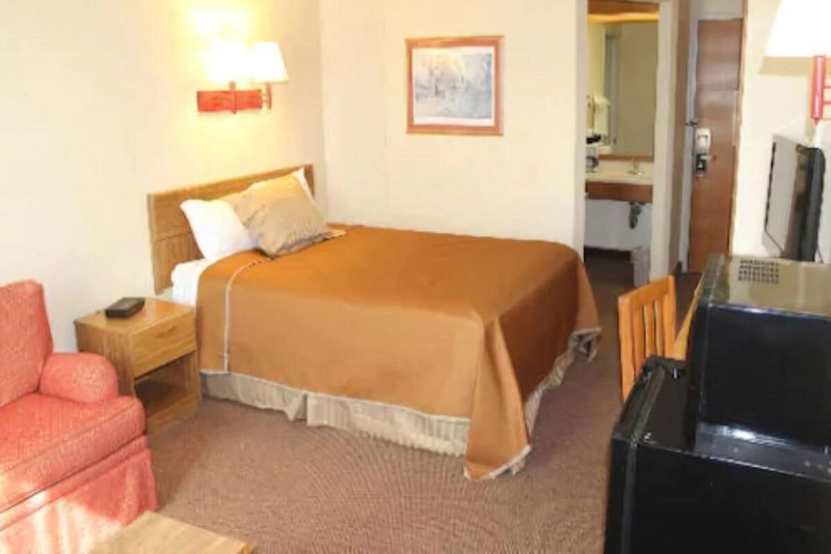 A hotel room with a bed, a desk, a chair, a television, and a bathroom visible through an open door.