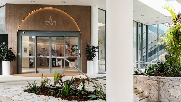 A modern hotel entrance with a stone facade, a glass door, and a staircase leading to an upper level. - Amora Hotel Brisbane (Spring Hill)