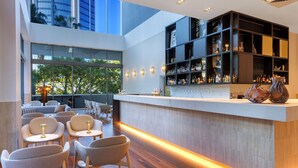 A modern bar area with a wooden floor, seating with round tables, and a bar counter with shelves of bottles. - Amora Hotel Brisbane (Spring Hill)