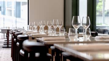 Une rangée de tables, avec des verres à vin et des assiettes vides, laisse supposer qu’il s’agit d’un espace réservé aux repas dans un restaurant.