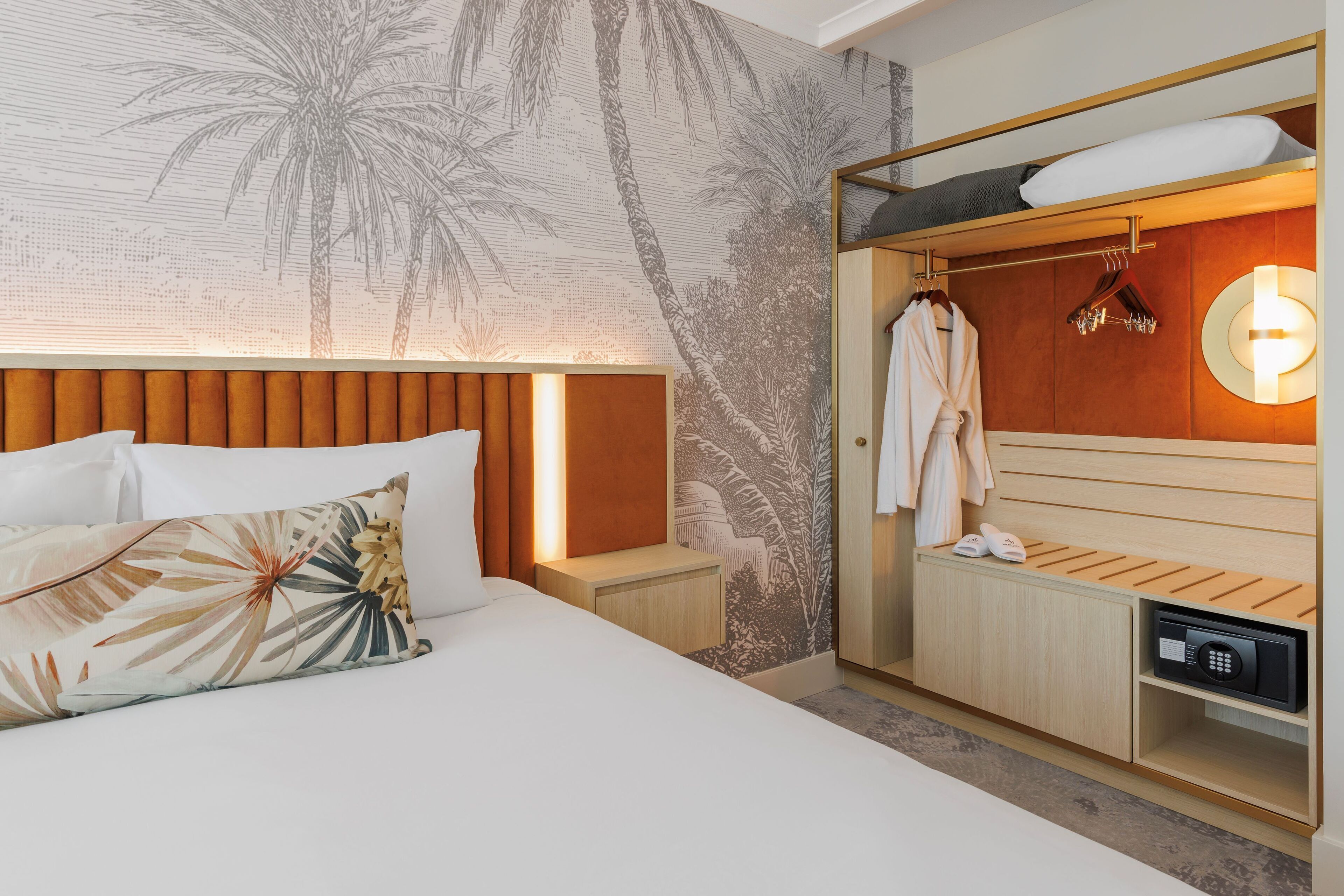 Una habitación de hotel con cama, mesita de noche, armario de madera, bata y zapatero.