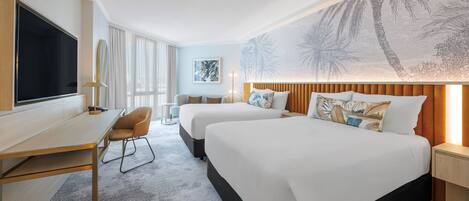 Une chambre d’hôtel avec deux lits, un bureau, une télévision et une grande fresque murale.