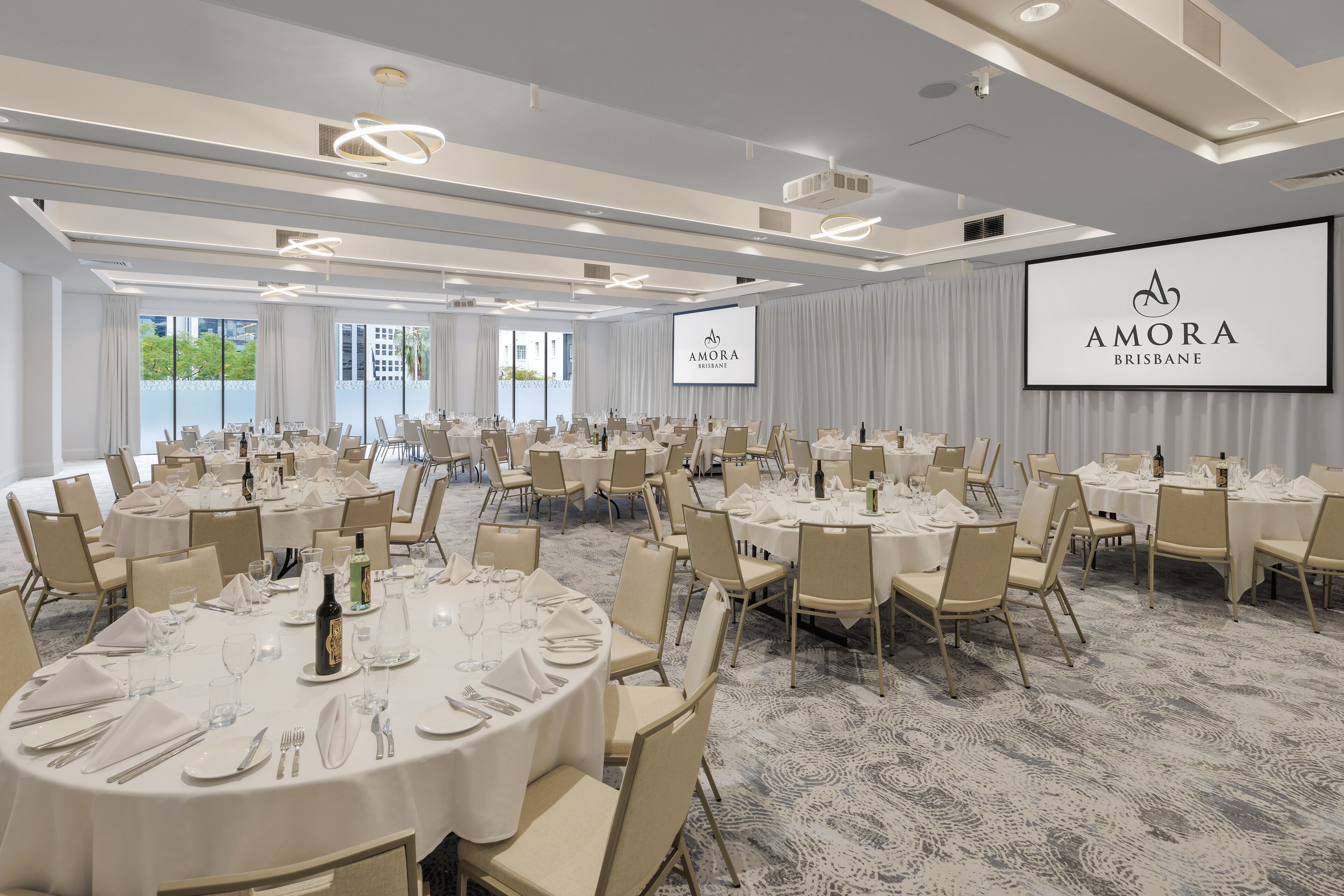 A conference room with round tables, chairs, and a large screen displaying the logo.