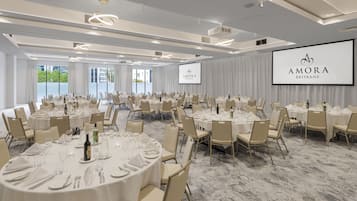 A conference room with round tables, chairs, and a large screen displaying the logo.