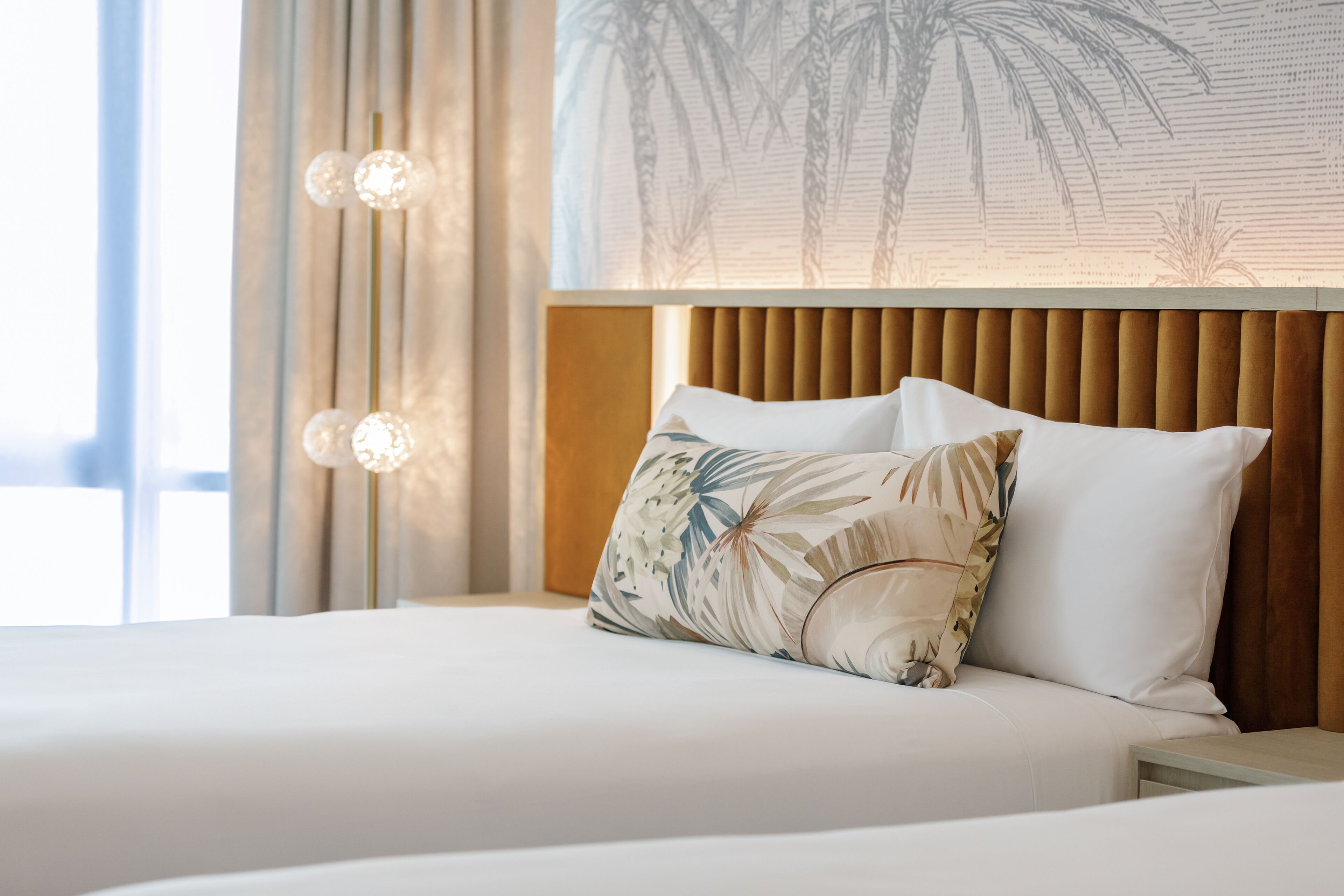 A hotel room with a bed, a nightstand, and a wall with a tropical plant design.