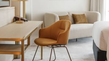 Ein Hotelzimmer mit einem Holztisch, einem modernen orangefarbenen Sessel, einer Couch mit Kissen und einem gerahmten Bild an der Wand.