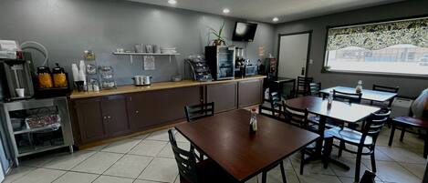 A restaurant with a counter, tables, chairs, and a television.