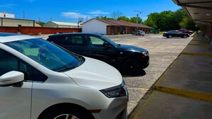A parking lot with several cars, a building with a red roof, and a clear blue sky. - Royal Inn & Suites (Mountain Grove)