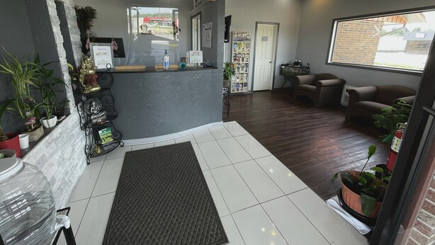 A reception area with a grey reception desk, a small seating area with two brown sofas, and a large window with a view of a brick building. - Royal Inn & Suites (Mountain Grove)
