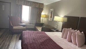 A hotel room with a large bed, a chair, a desk, and a lamp. - Royal Inn & Suites (Mountain Grove)