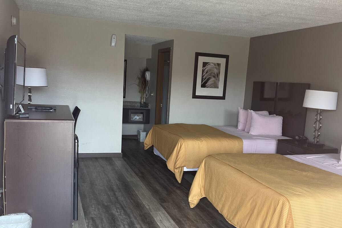 A hotel room with two beds, a desk, a chair, a dresser, and a bathroom visible through an open door.