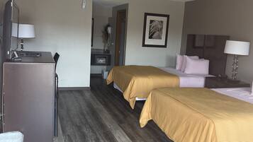 A hotel room with two beds, a desk, a chair, a dresser, and a bathroom visible through an open door.