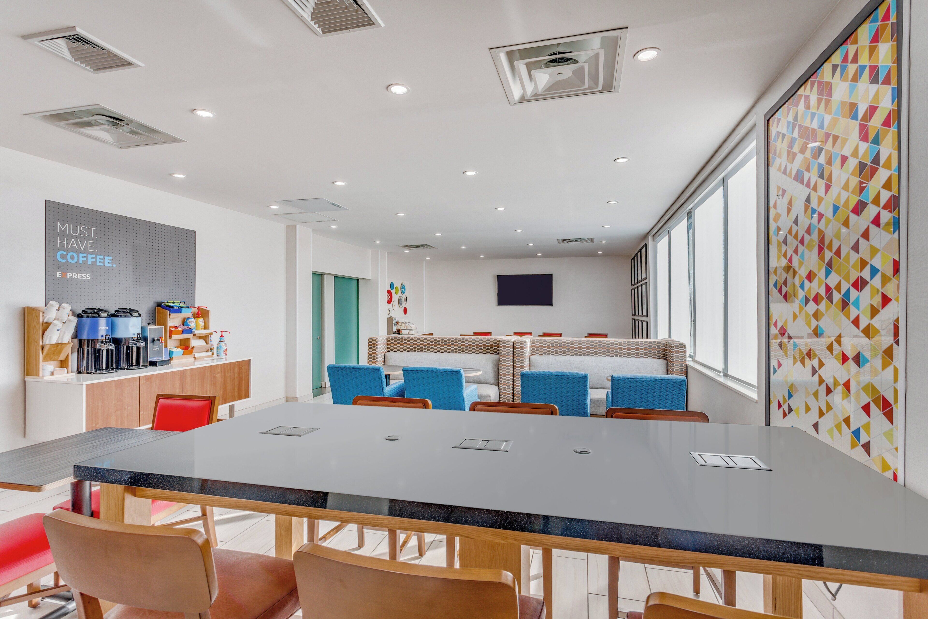 Uma sala de reuniões moderna com uma mesa comprida, cadeiras, um cantinho de café e uma janela grande.
