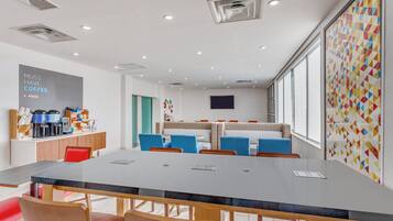 Uma sala de reuniões moderna com uma mesa comprida, cadeiras, um cantinho de café e uma janela grande.
