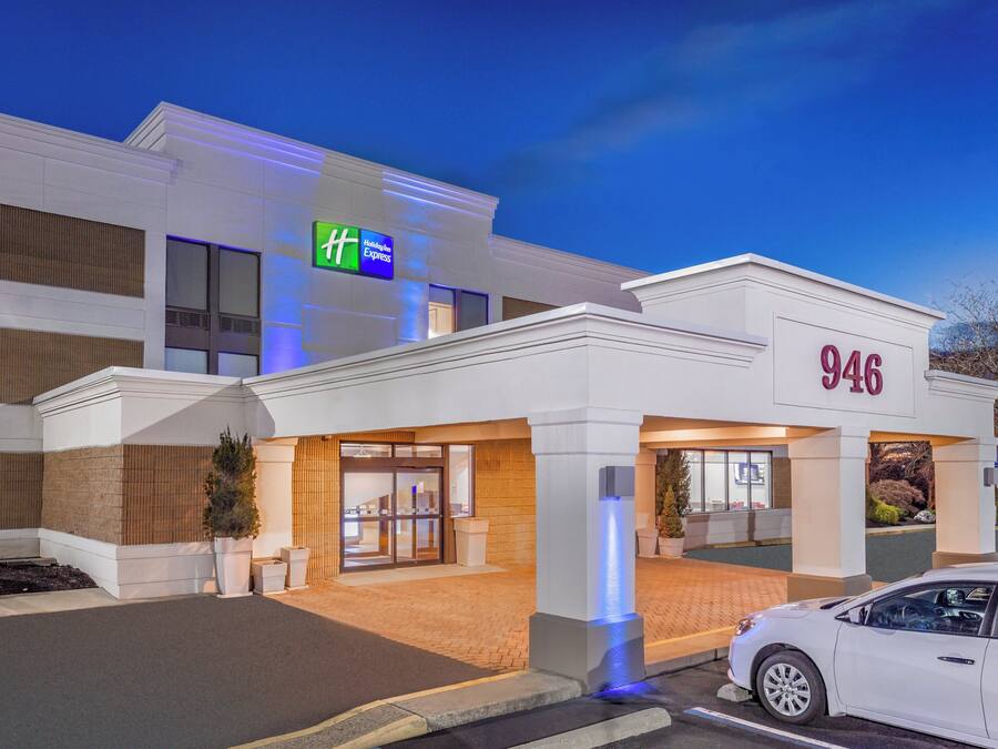 Een Holiday Inn Express gebouw met een moderne gevel, een parkeerplaats en een witte auto ervoor geparkeerd.