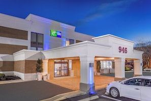 A Holiday Inn Express building with a modern facade, a parking lot, and a white car parked in front. - Holiday Inn Express Ramsey-Mahwah by IHG (Ramsey)