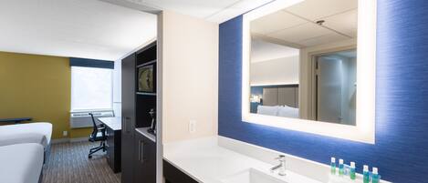 Habitación de hotel con un espejo grande, un lavamanos blanco y una mesita de noche con artículos de aseo.