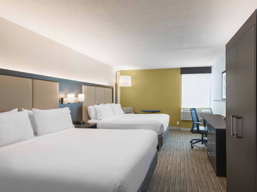 A hotel room with two beds, a desk, a chair, a lamp, and a window.