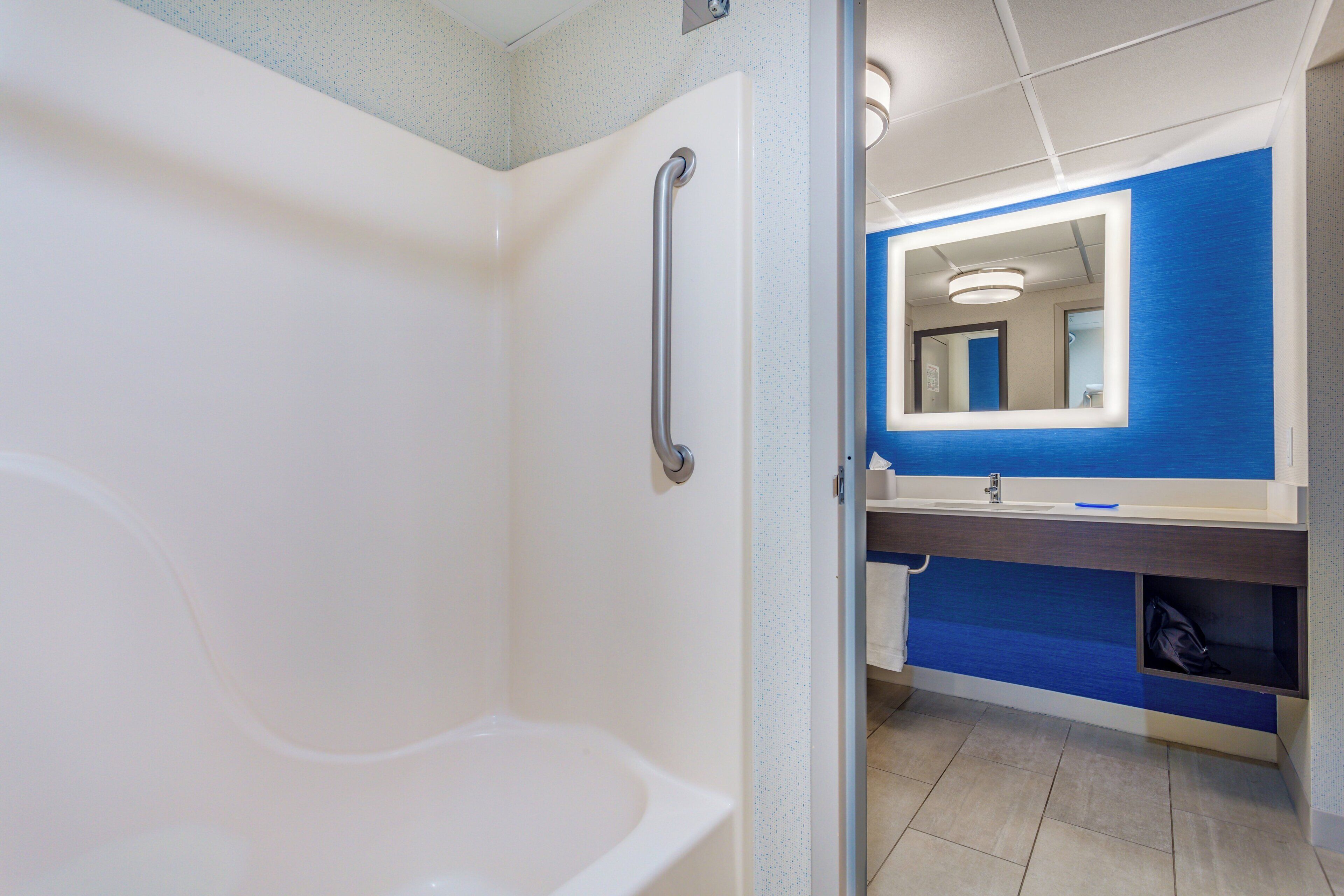 A bathroom with a white bathtub, a blue vanity, and a mirror.